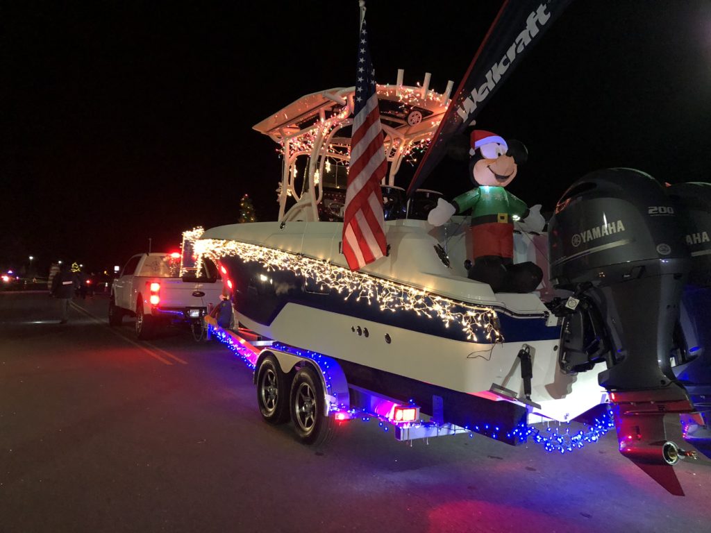 Boat float pulled by truck in parade with lights , flag and mickey mouse