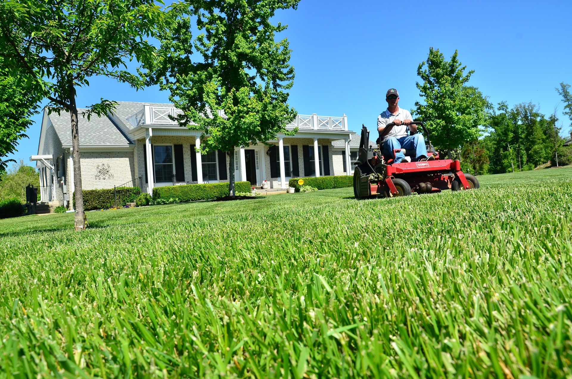 man mowing grass on riding lawnmower with house in background