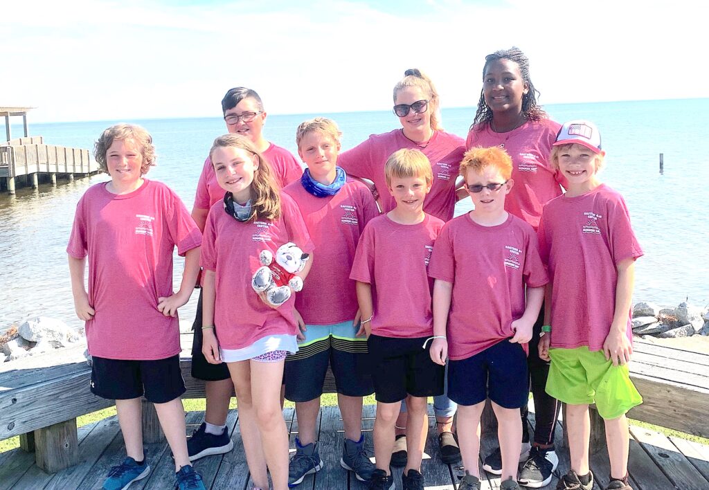 Nine children in pink camp shirts near water