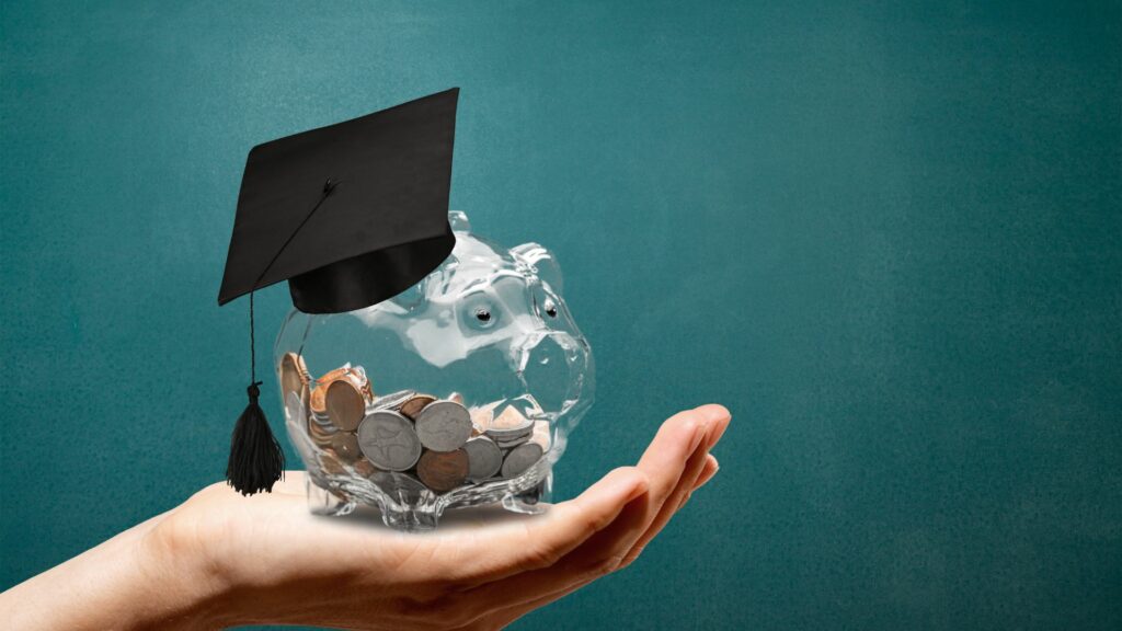 Hand holding clear glass piggy bank wearing graduation cap